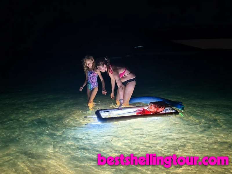 A mother and daughter shelling in shallow water at night beside the LED light pod on a night shelling tour in Florida