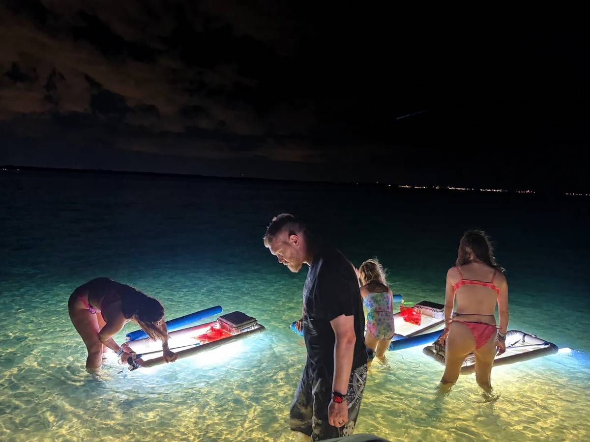 Guests shelling in shallow, calm water at night beside glowing LED light pods on a Fun Florida Tours night shelling and snorkeling tour